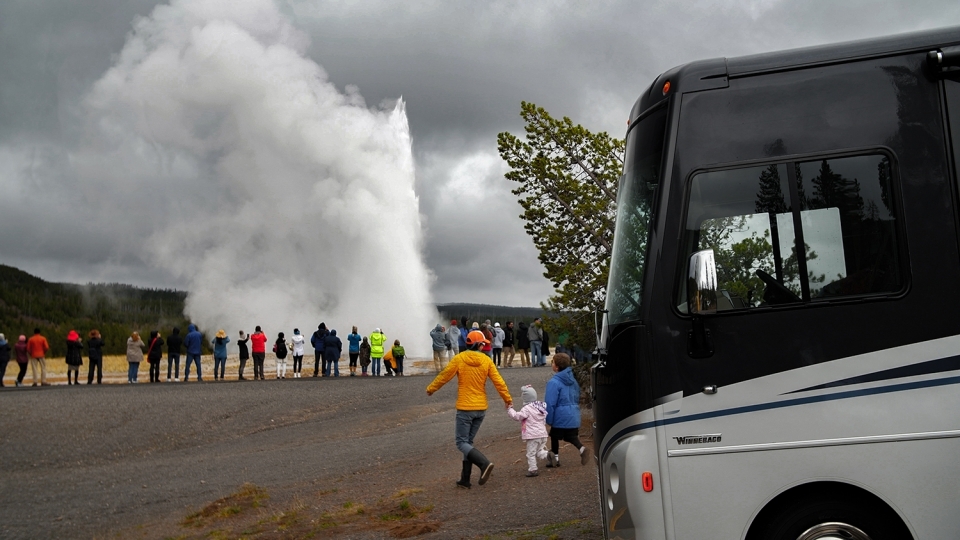 A family walks from their parked Winnebago to view Old Faithful erupting at Yellowstone National Park