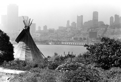 Black and white photo of teepee on Alcatraz with skyline of San Francisco in the background