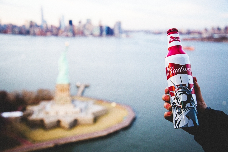 Statue of Liberty packaging on Budweiser bottle, held in frame with Statue of Liberty National Monument in the distance
