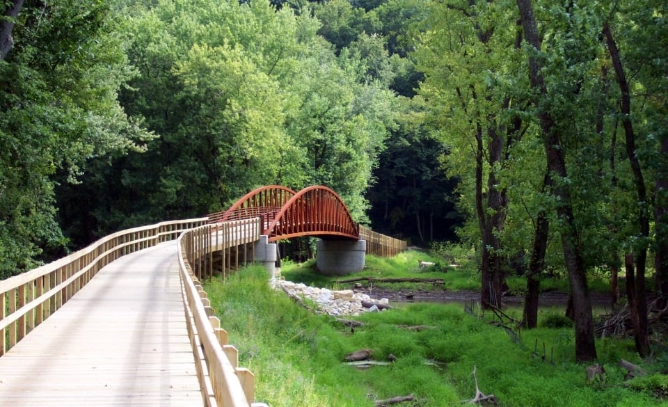 A wooden boardwalk with a red bridge over a stream in the green woods at Effigy Mounds National Monument in Iowa