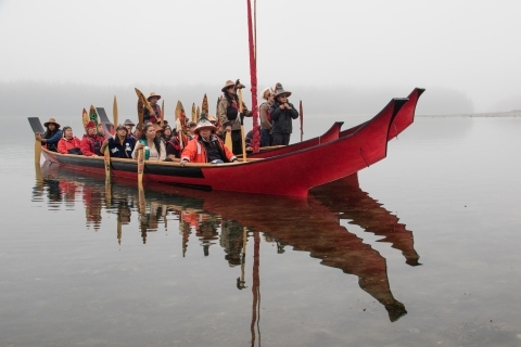 A group of people travel across water in a long, red canoe