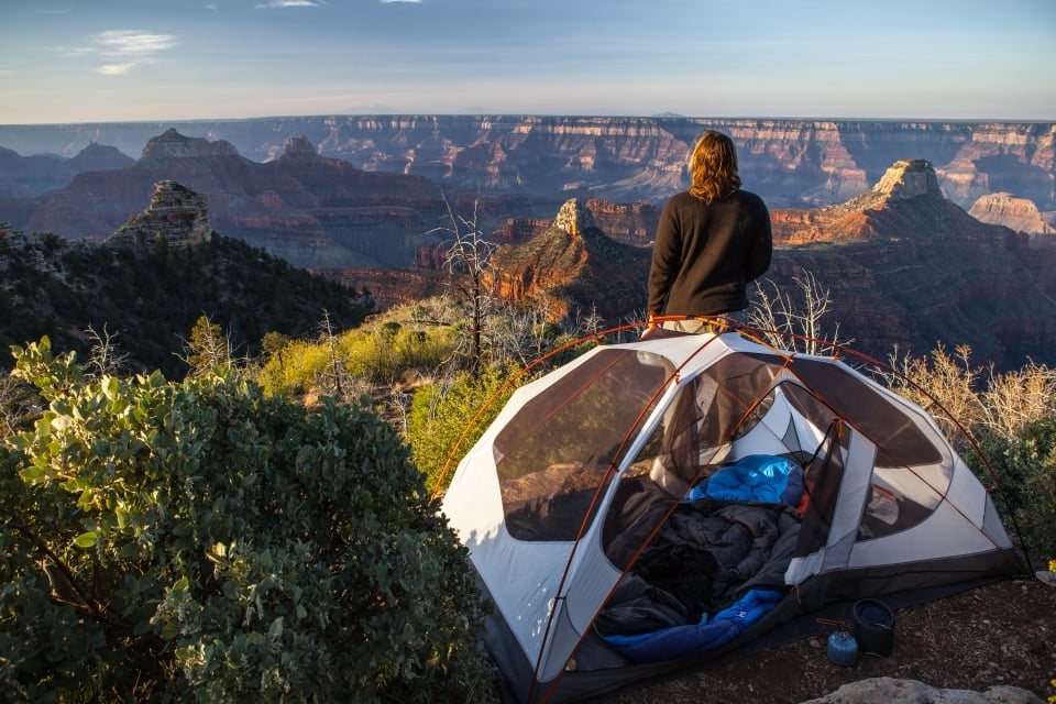 A person standing next to a tent watching Grand Canyon National Park light up during sunrise