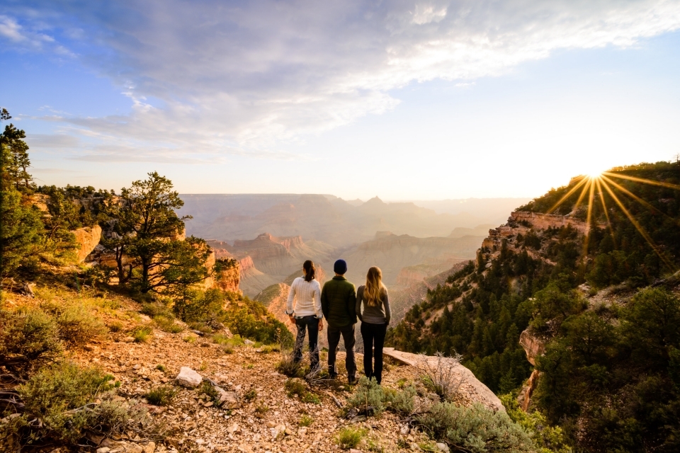 Three people standing at the edge of a cliff at Grand Canyon National Park