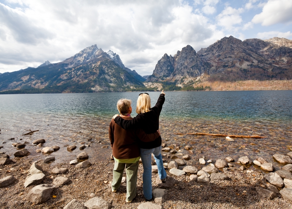 Two women looking out on Grand Teton National Park, one with her arm around the other and one arm pointing outwards.