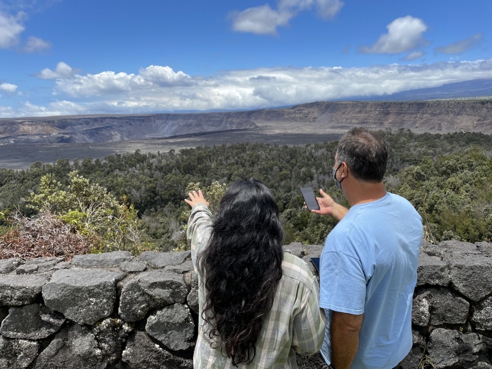 Two visitors standing at an overlook pointing towards a volcanic crater