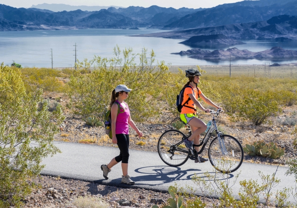 Hiker and cyclist on paved trail, lake and mountains in background