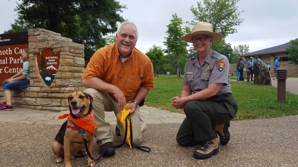 A dog sitting with his owner and a park ranger outside the Mammoth Cave National Park Visitor Center