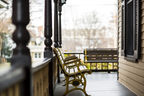 A painted porch in a warm light. Two wooden and metal benches sit on the porch