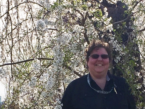 Megan Springate smiles in front of blooming cherry blossom trees