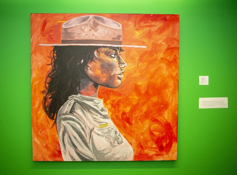 Painting against a bright green wall, depicting a woman in a park ranger uniform and hat, looking to the right.