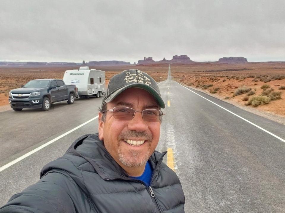 Robert Morales takes a selfie in front of his RV and car on an open road