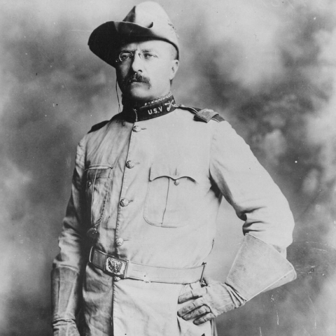 Black and white portrait photograph of Theodore Roosevelt standing, in full Rough Rider U.S.V uniform