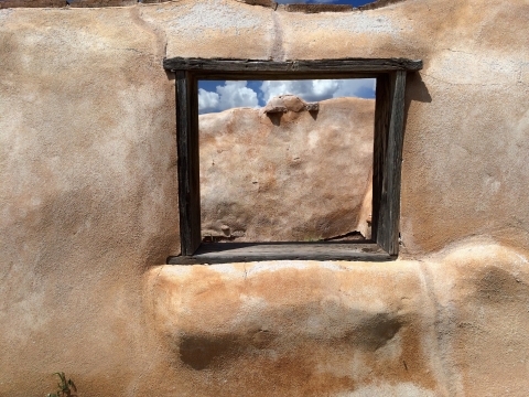 A small window in a stone wall shows another stone wall in the near distance