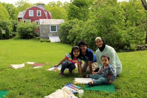 A women and three children sitting on blanket in a field creating art with watercolor paints.