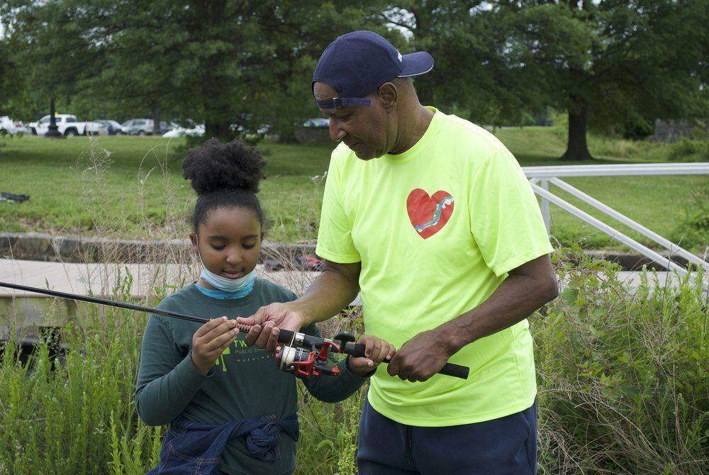 Bruce Holmes works with Anacostia youth and shows her how to cast a rod during Anacostia Park's Community Fishing Program